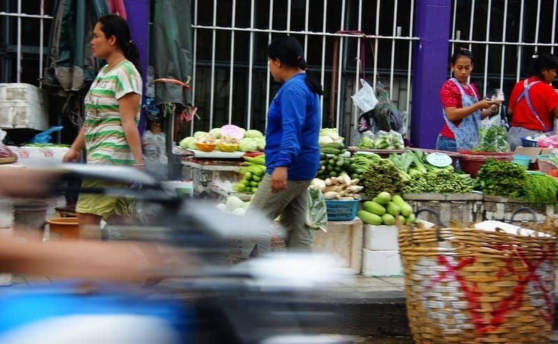 Thai ladies set up market just as a motorist zooms past them on the street - Bangkok, Thailand