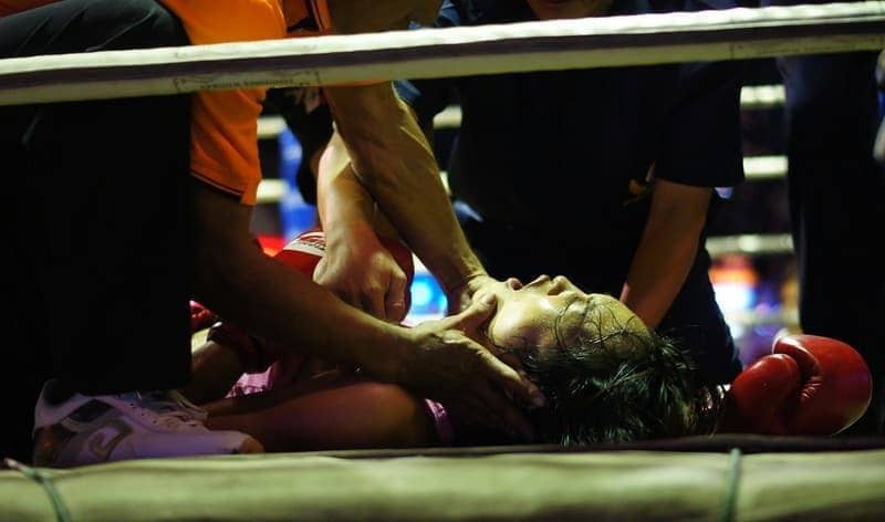 A female Muay Thai boxer surrounded by trainers gasps for breathe after being rendered unconscious 