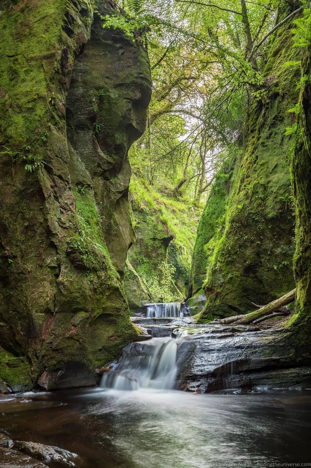 The reddish water and mossy walls of the Devil's Pulpit gorge at Finnich Glen