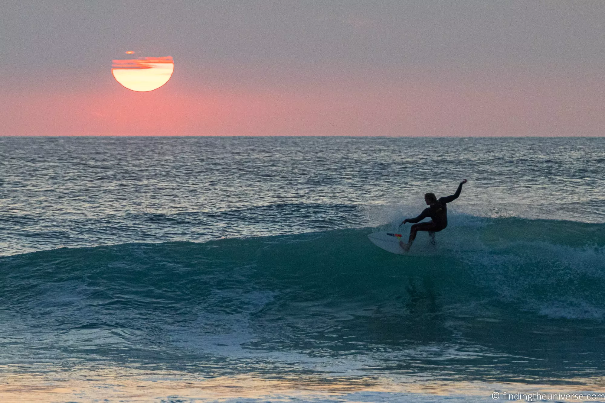A surfer in the water at sunset on a Cornwall beach