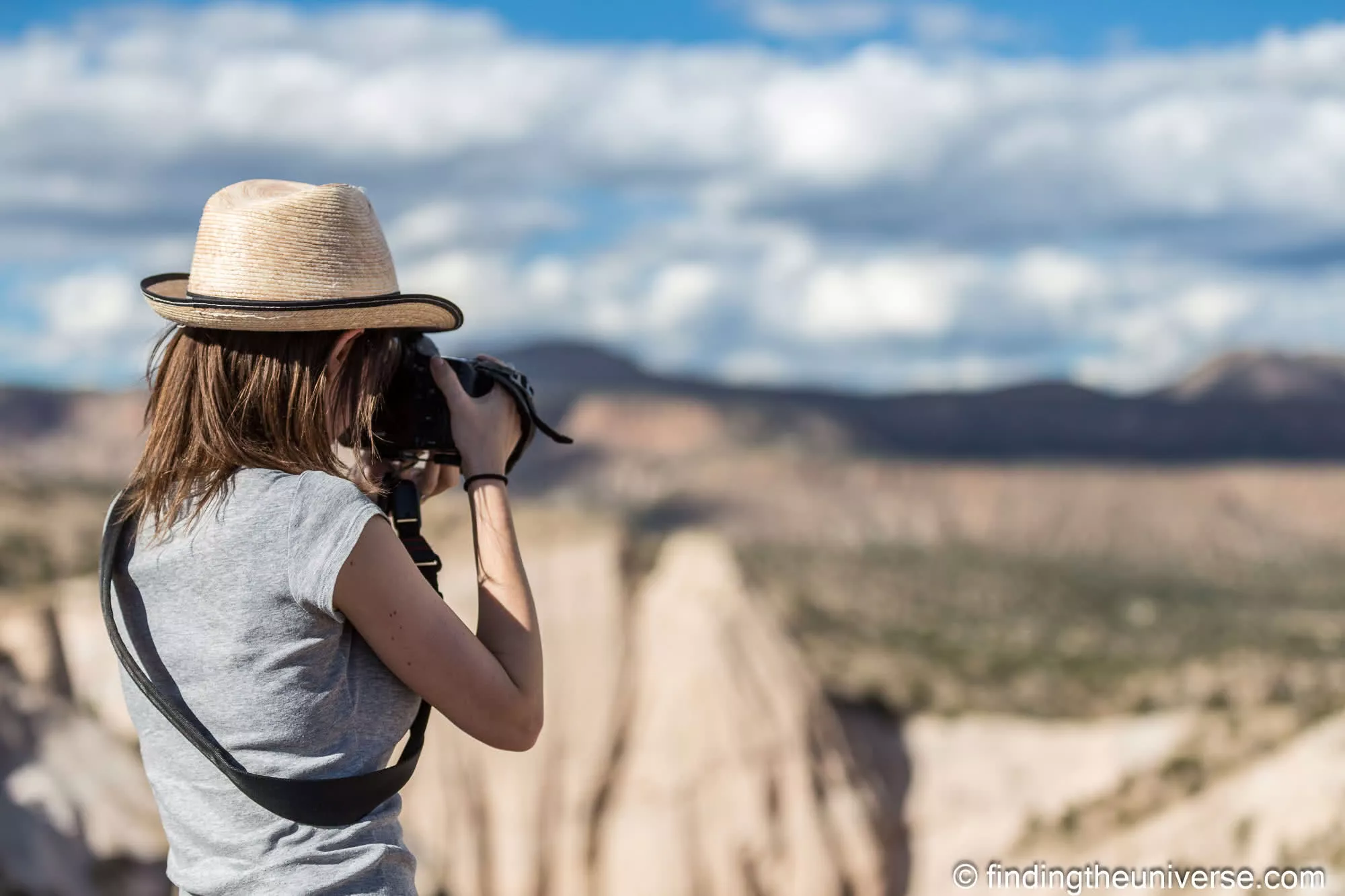 A photographer in a straw hat shooting a canyon, the canyon soft and out of focus behind her at f/2.8