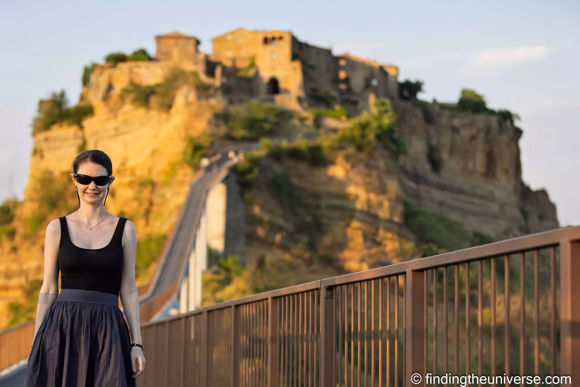 Jess in the foreground, sharp, with an Italian hill town softened to a blur behind her at f/2.8