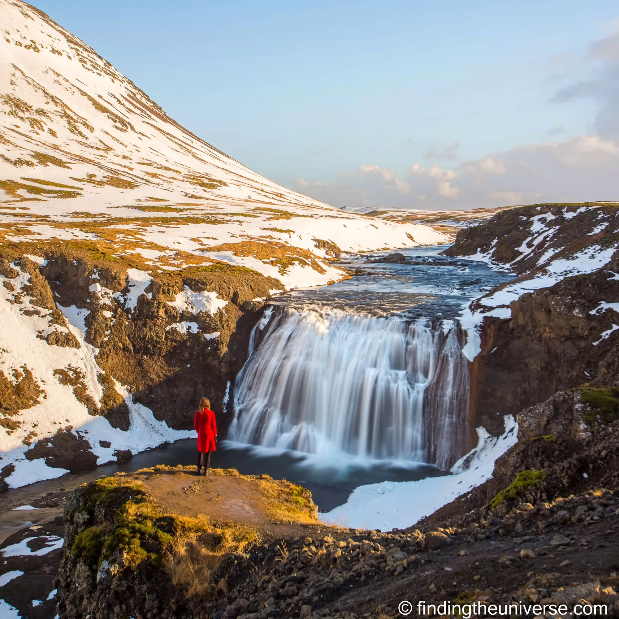 Þórufoss waterfall in Iceland with a small figure in red on a snowy ledge, sharp from front to back