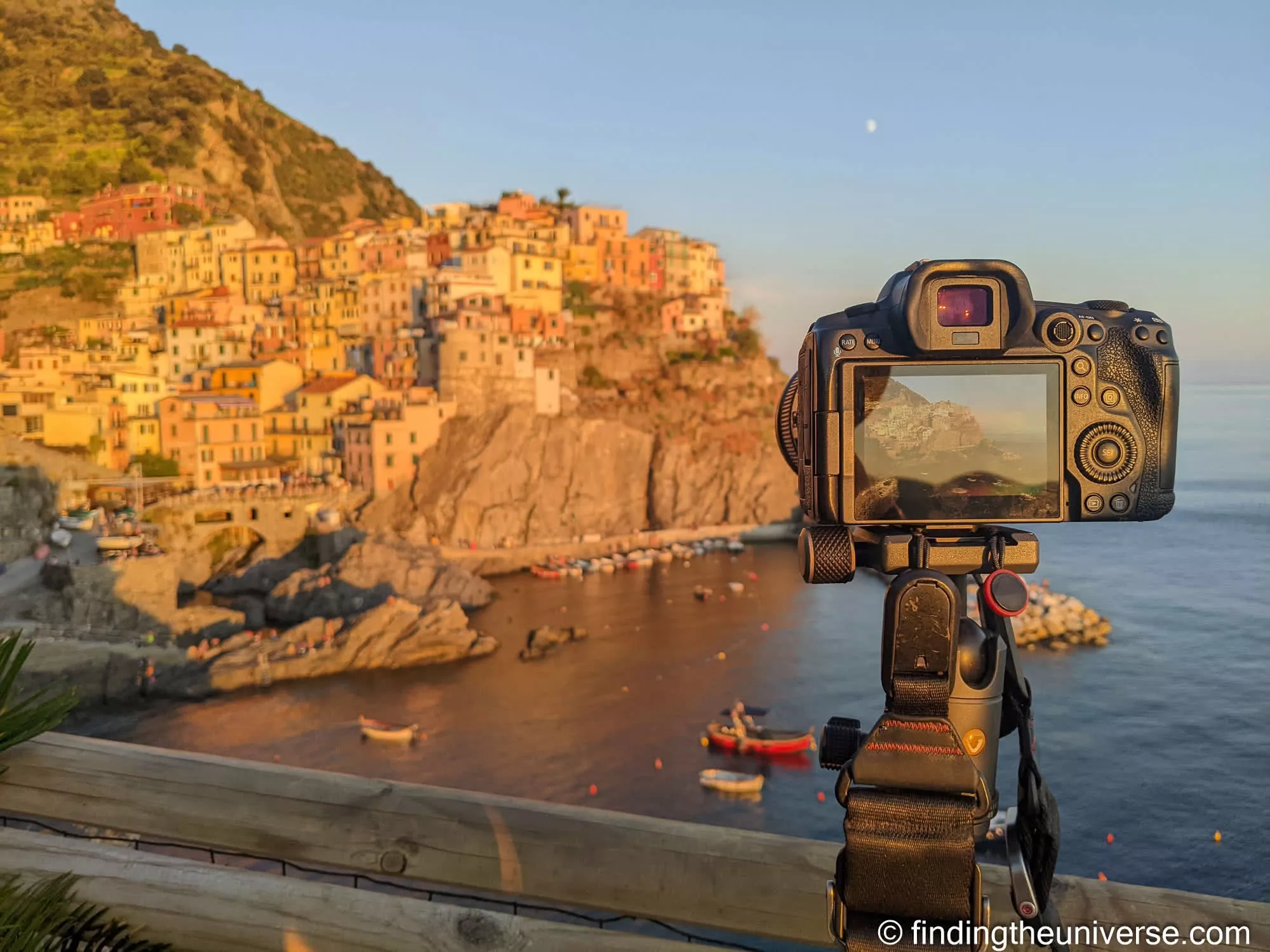 A camera on a tripod framing Manarola at golden hour