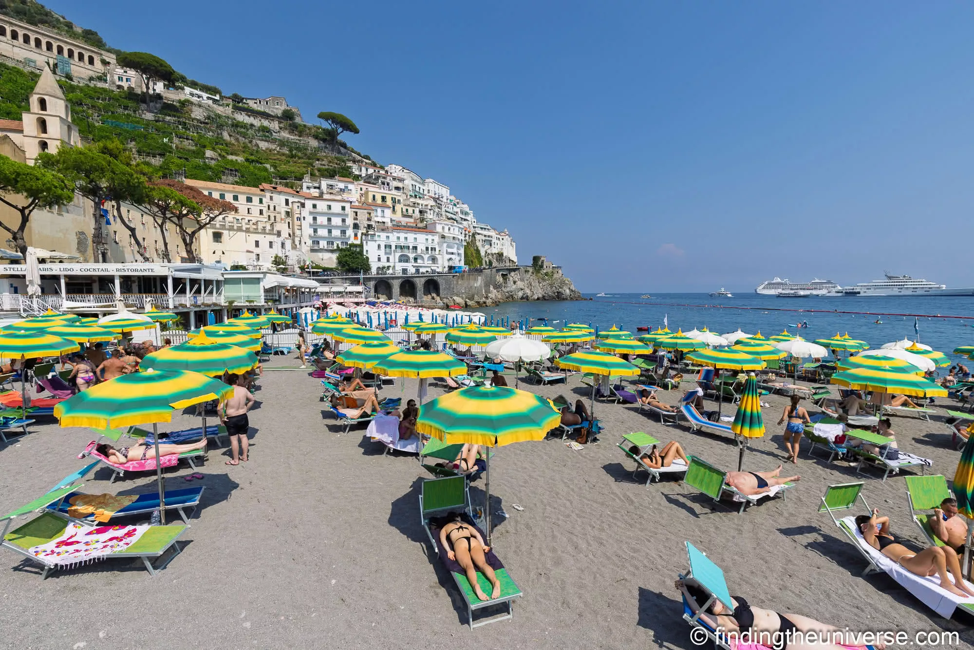 Rows of green and yellow parasols on Amalfi's beach below the town