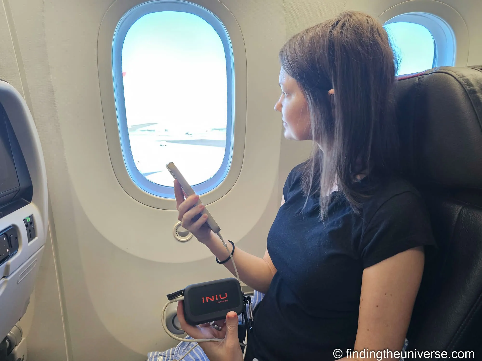 Jess holding the INIU RG-10000 while charging her phone on a plane at Philadelphia airport