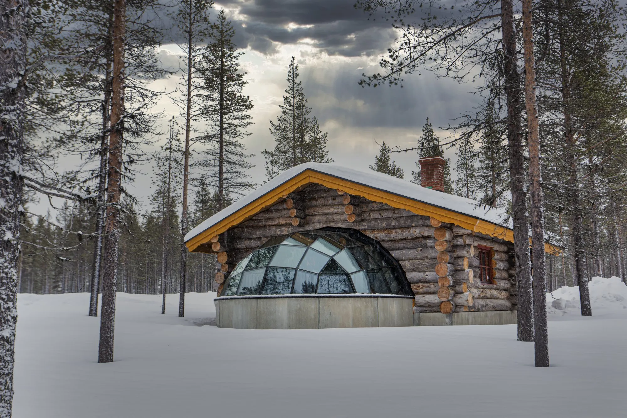Log cabin and glass igloo in a snowy forest in Finnish Lapland
